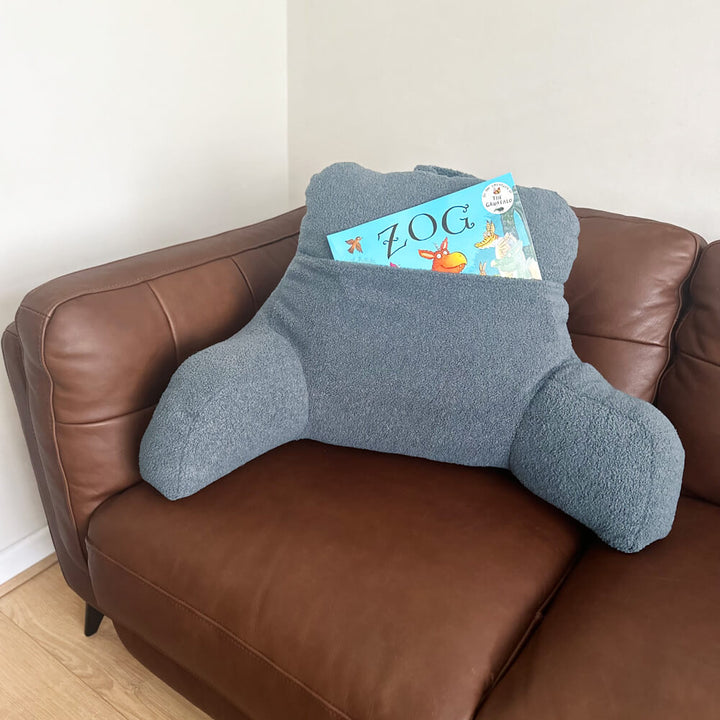 Light Blue teddy fleece reading cushion with a large pocket which has a children's book in the pocket (not included). The reading cushion is on a brown leather couch (not included)
