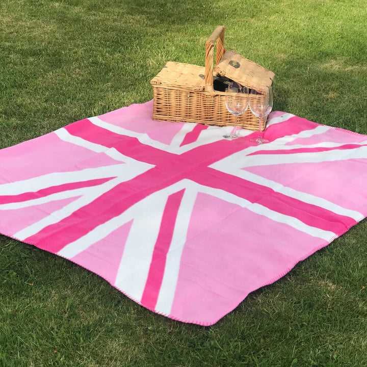 Pink and white union jack 127cm x 152cm fleece blanket outside on grass with a picnic basket