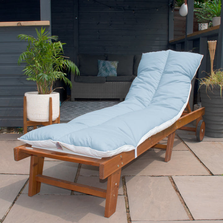 Lancashire Textiles Sky Blue Sun Lounger Topper on a wooden sun lounger in a garden. 
